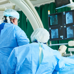 Image of Two healthcare workers in surgical gowns and caps perform an interventional radiology procedure on a patient.